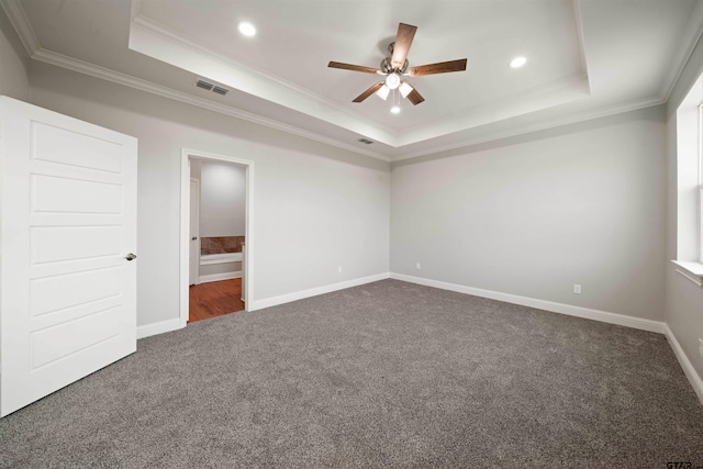 unfurnished bedroom featuring ornamental molding, ensuite bathroom, ceiling fan, a tray ceiling, and dark carpet