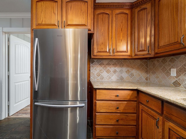 kitchen featuring dark hardwood / wood-style flooring, tasteful backsplash, light stone counters, crown molding, and stainless steel refrigerator