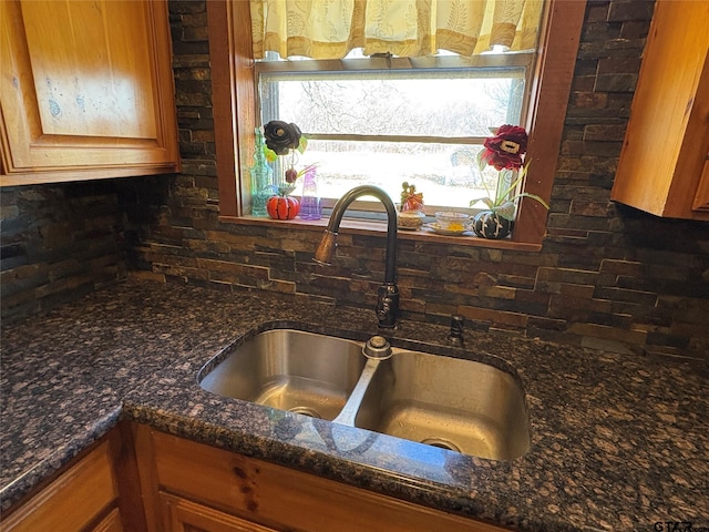 kitchen featuring dark stone counters, brown cabinets, a sink, and decorative backsplash