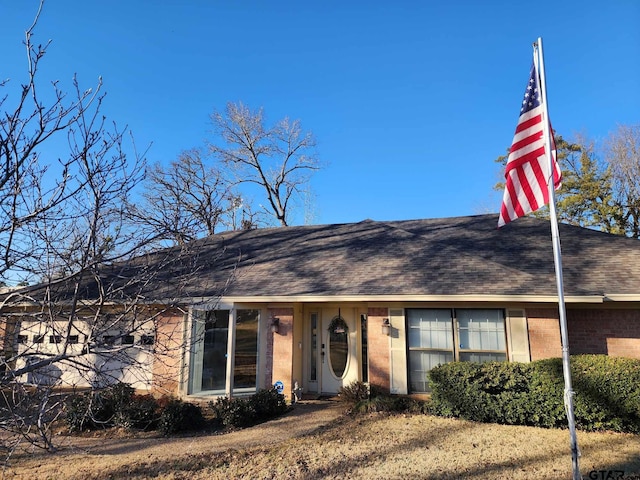 view of front facade featuring brick siding and roof with shingles