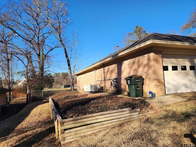 view of home's exterior featuring brick siding, an attached garage, central AC, and fence