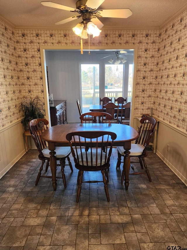 dining room featuring a wainscoted wall, a textured ceiling, crown molding, and wallpapered walls