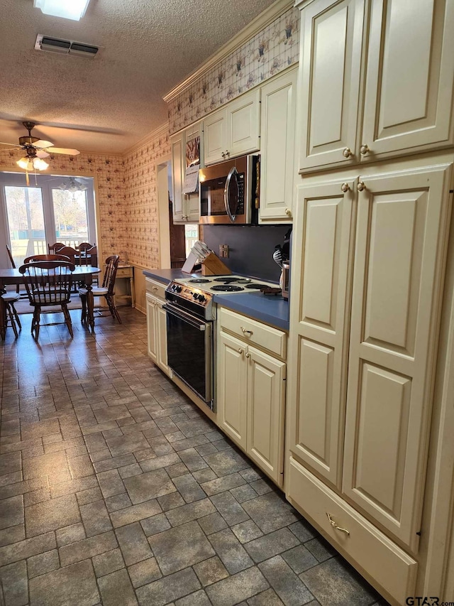 kitchen featuring ceiling fan, range with electric stovetop, ornamental molding, a textured ceiling, and cream cabinetry