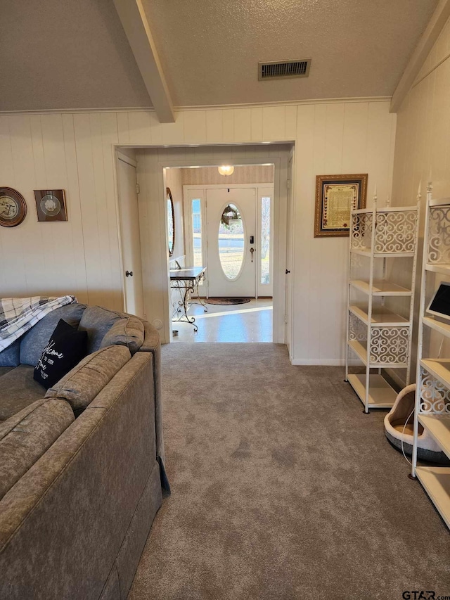 living room with beam ceiling, carpet floors, a textured ceiling, and wood walls