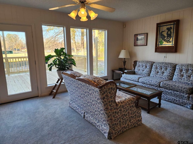 living room with ceiling fan, carpet flooring, a textured ceiling, and wood walls