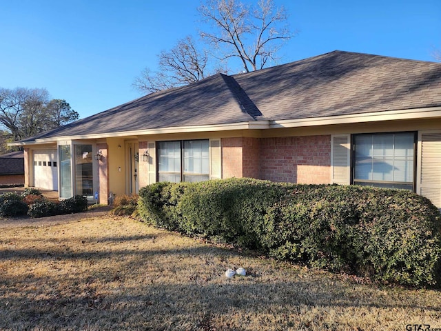 ranch-style house with a front yard, brick siding, an attached garage, and a shingled roof