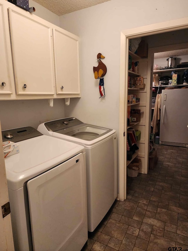 washroom featuring cabinets, a textured ceiling, and washing machine and clothes dryer