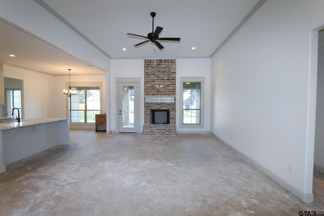 unfurnished living room featuring a fireplace, ceiling fan with notable chandelier, ornamental molding, and sink