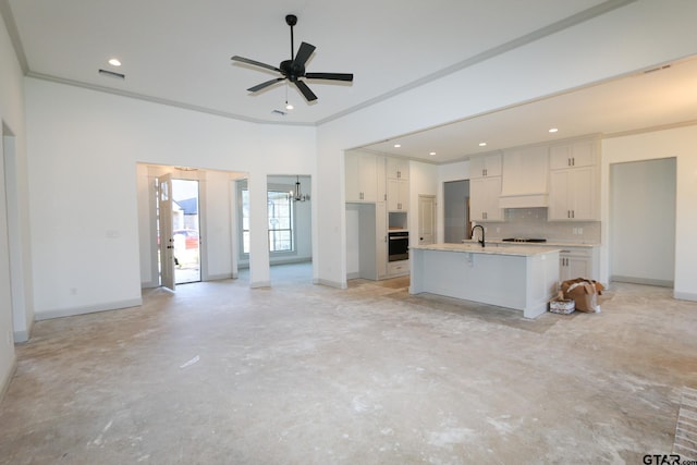 kitchen with premium range hood, white cabinets, ceiling fan with notable chandelier, an island with sink, and wall oven