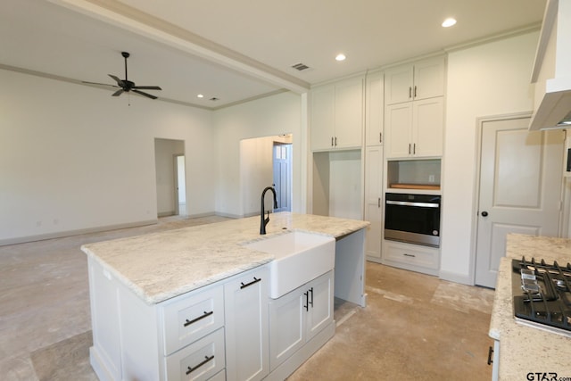 kitchen with light stone counters, stainless steel appliances, ceiling fan, a kitchen island with sink, and sink