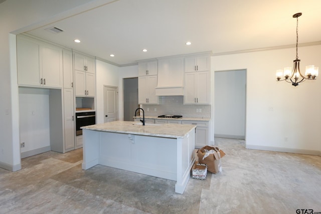 kitchen with gas stovetop, white cabinets, oven, hanging light fixtures, and an island with sink