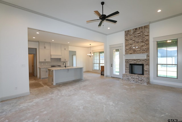 unfurnished living room featuring ceiling fan with notable chandelier, ornamental molding, sink, and a brick fireplace