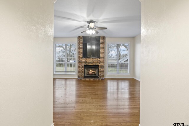 unfurnished living room featuring ceiling fan, plenty of natural light, a fireplace, and dark hardwood / wood-style flooring