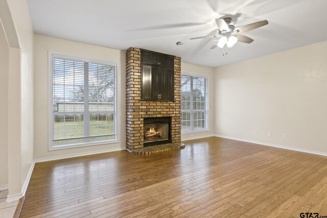 unfurnished living room featuring ceiling fan, hardwood / wood-style floors, and a brick fireplace