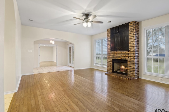 unfurnished living room featuring ceiling fan, a brick fireplace, and light hardwood / wood-style flooring