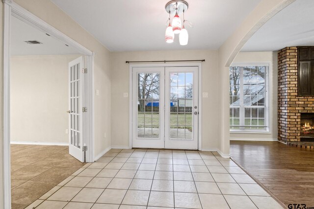 entryway featuring light tile patterned floors, a fireplace, and french doors