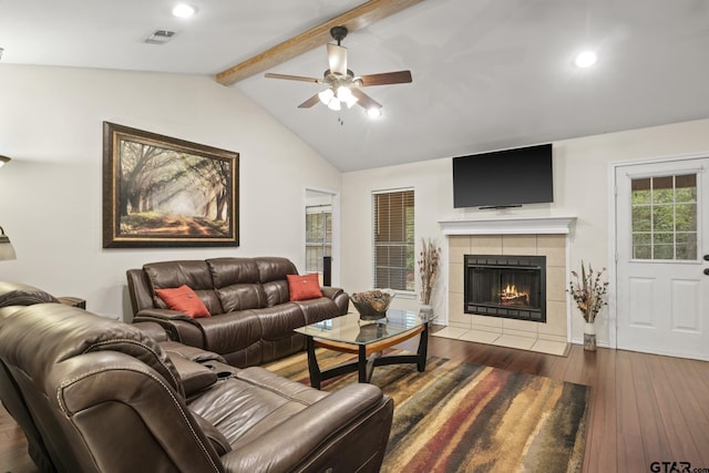 living room with a tiled fireplace, ceiling fan, dark hardwood / wood-style flooring, and lofted ceiling with beams