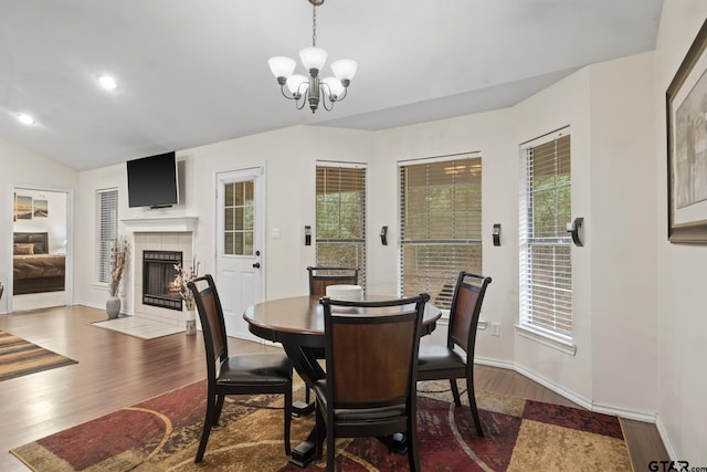 dining space featuring a tiled fireplace, a wealth of natural light, dark wood-type flooring, and a notable chandelier