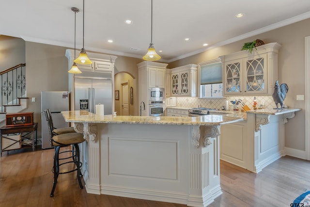 kitchen with hanging light fixtures, built in appliances, a breakfast bar, a kitchen island, and light wood-type flooring