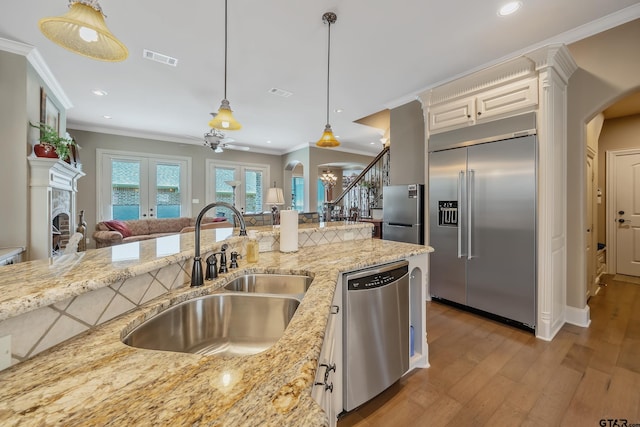 kitchen with light stone countertops, sink, light hardwood / wood-style flooring, pendant lighting, and appliances with stainless steel finishes