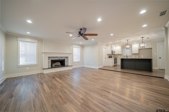 unfurnished living room with a fireplace, sink, ornamental molding, ceiling fan, and wood-type flooring