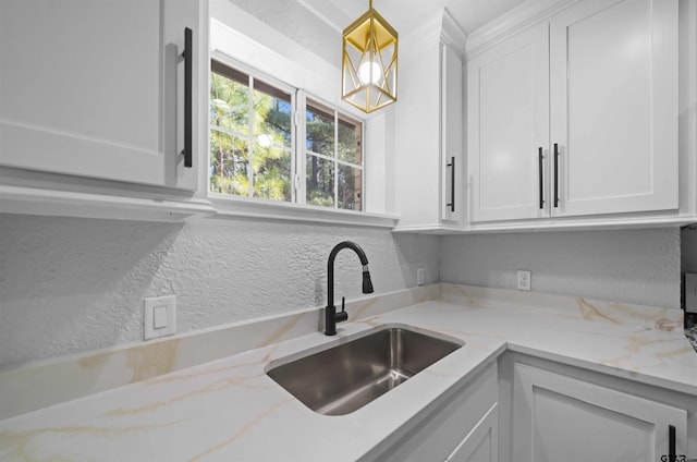 kitchen featuring sink, light stone countertops, white cabinets, and pendant lighting