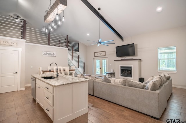 kitchen with light stone counters, a kitchen island with sink, high vaulted ceiling, white cabinetry, and light wood-type flooring