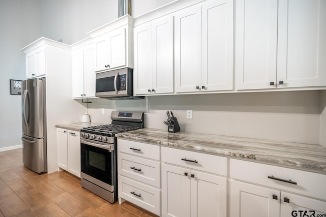 kitchen with stainless steel appliances, light hardwood / wood-style floors, white cabinetry, and light stone countertops