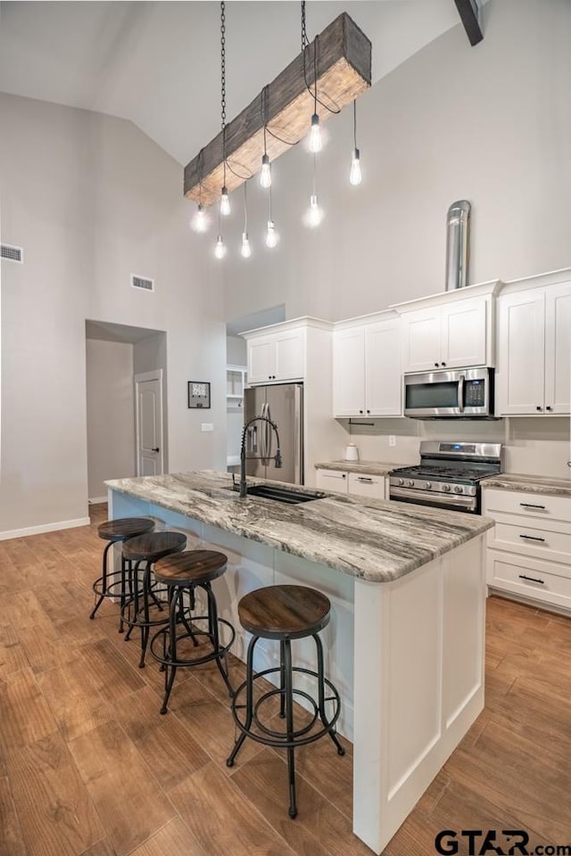 kitchen featuring high vaulted ceiling, white cabinets, a center island with sink, and stainless steel appliances