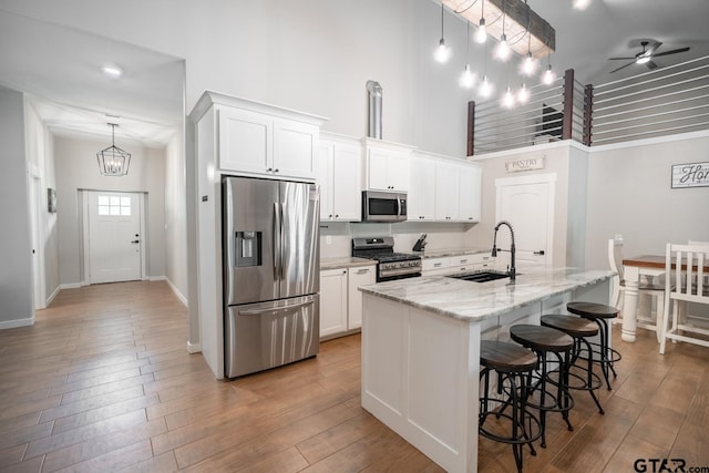 kitchen with stainless steel appliances, a towering ceiling, white cabinetry, and a kitchen island with sink