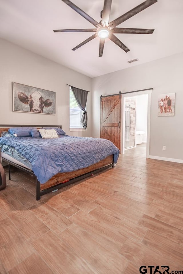 bedroom featuring a barn door, ceiling fan, connected bathroom, and wood-type flooring