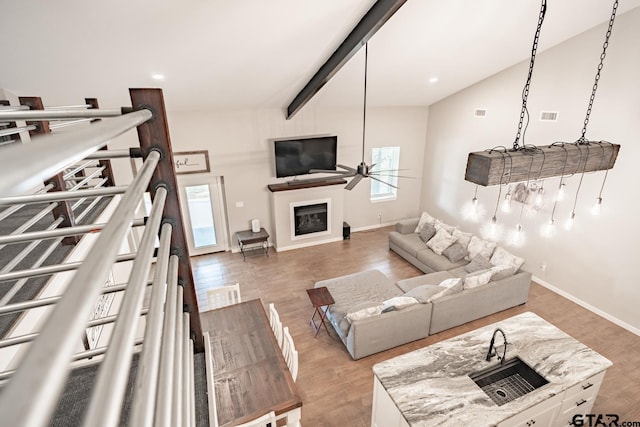 living room with hardwood / wood-style flooring, ceiling fan, sink, and vaulted ceiling with beams