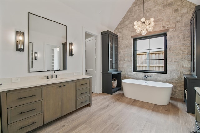 3312 Forest Ct, Tyler, TX 75703 - bathroom featuring vaulted ceiling, vanity, a freestanding tub, wood finished floors, and a chandelier