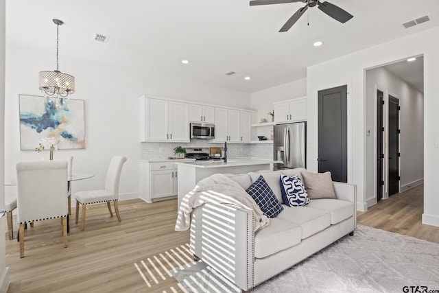 living room with ceiling fan with notable chandelier and light wood-type flooring