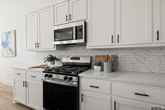 kitchen featuring white cabinetry, stainless steel appliances, light stone counters, tasteful backsplash, and light wood-type flooring