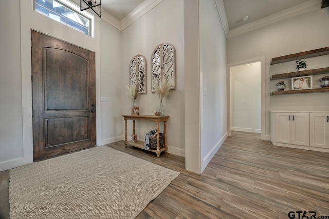 foyer entrance with a towering ceiling, a notable chandelier, crown molding, and light hardwood / wood-style flooring