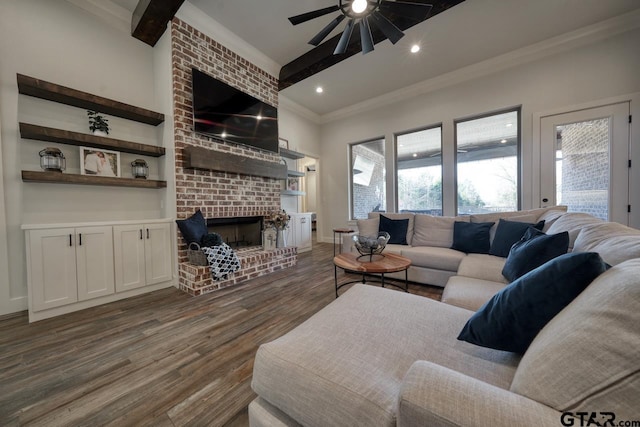 living room with ceiling fan, a brick fireplace, dark hardwood / wood-style floors, crown molding, and beam ceiling