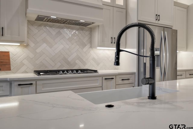 kitchen with white cabinets, stainless steel gas stovetop, backsplash, and light stone countertops