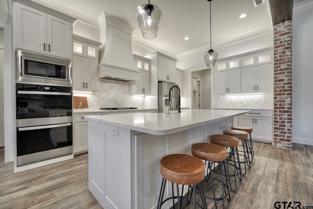 kitchen featuring stainless steel appliances, custom exhaust hood, white cabinetry, and an island with sink