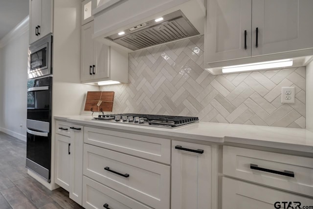 kitchen featuring dark hardwood / wood-style floors, stainless steel appliances, wall chimney range hood, decorative backsplash, and white cabinetry