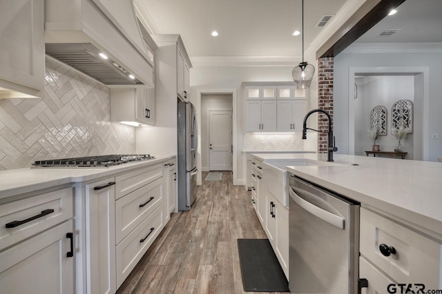 kitchen featuring appliances with stainless steel finishes, hanging light fixtures, premium range hood, white cabinets, and backsplash