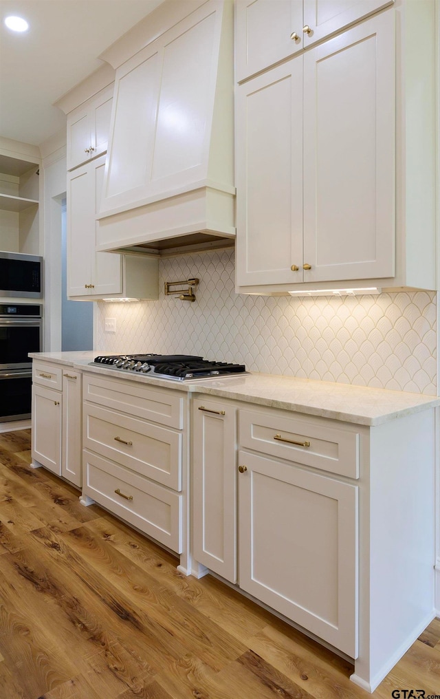 kitchen with decorative backsplash, light hardwood / wood-style floors, stainless steel gas stovetop, and premium range hood