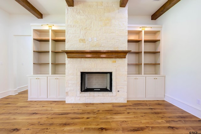 unfurnished living room with beamed ceiling, a stone fireplace, and light wood-type flooring