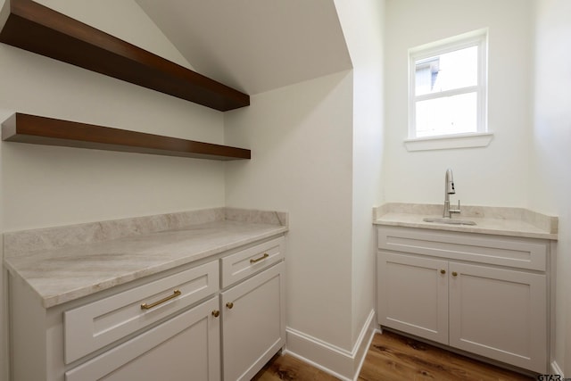 bar with white cabinetry, dark hardwood / wood-style flooring, light stone countertops, sink, and vaulted ceiling