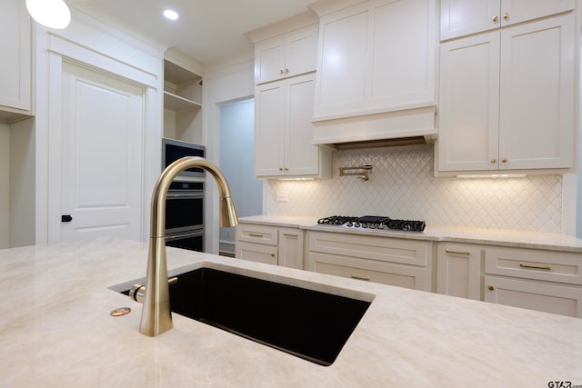 kitchen with tasteful backsplash, white cabinetry, stainless steel gas cooktop, and sink