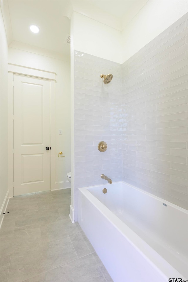 bathroom with tile patterned flooring, tiled shower / bath, and toilet