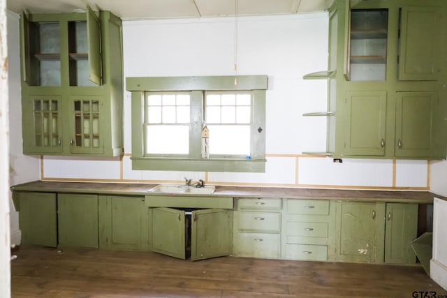 kitchen with glass insert cabinets, dark wood-type flooring, a sink, and green cabinets