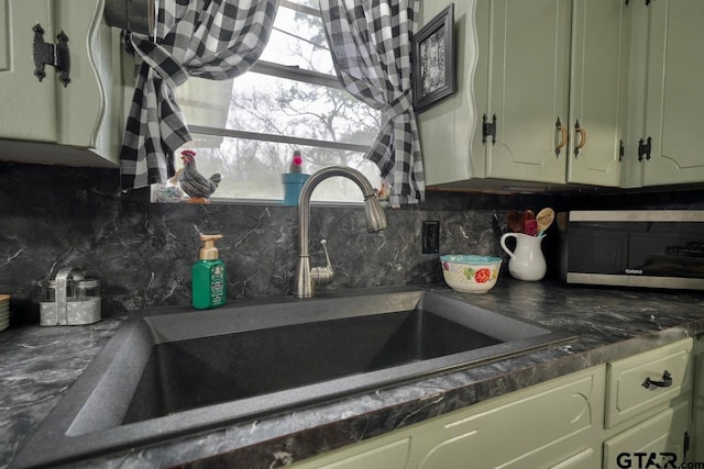 kitchen featuring backsplash, dark countertops, and a sink