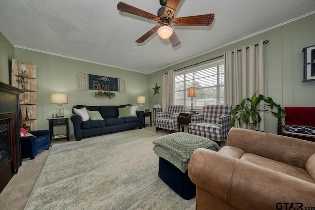 living room with carpet, ornamental molding, a glass covered fireplace, a ceiling fan, and a textured ceiling