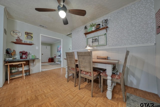 dining space with wallpapered walls, visible vents, wainscoting, ornamental molding, and a textured ceiling